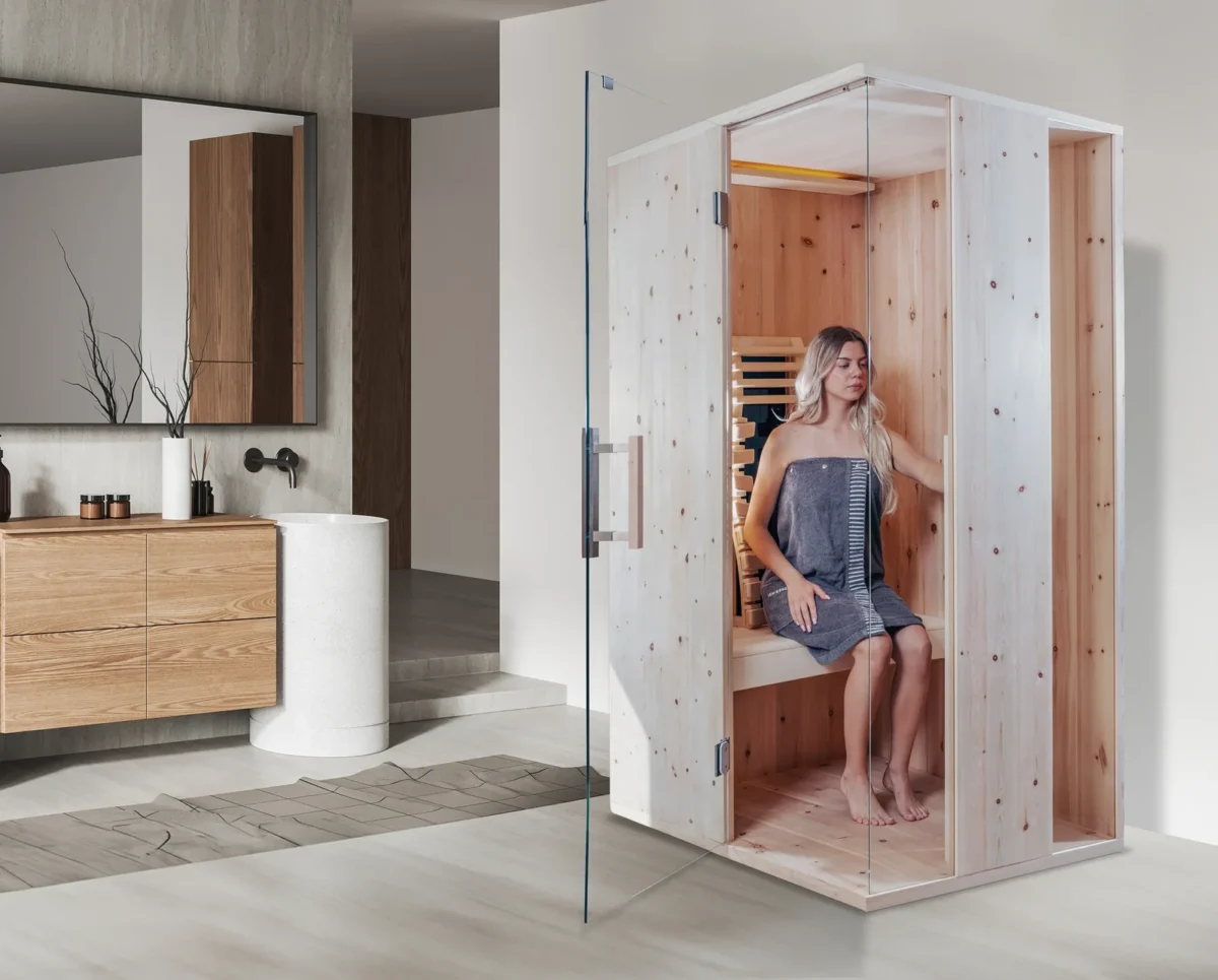 Infrarotkabine mit Glasfront in einem Badezimmer, eine Frau sitzt auf der Bank